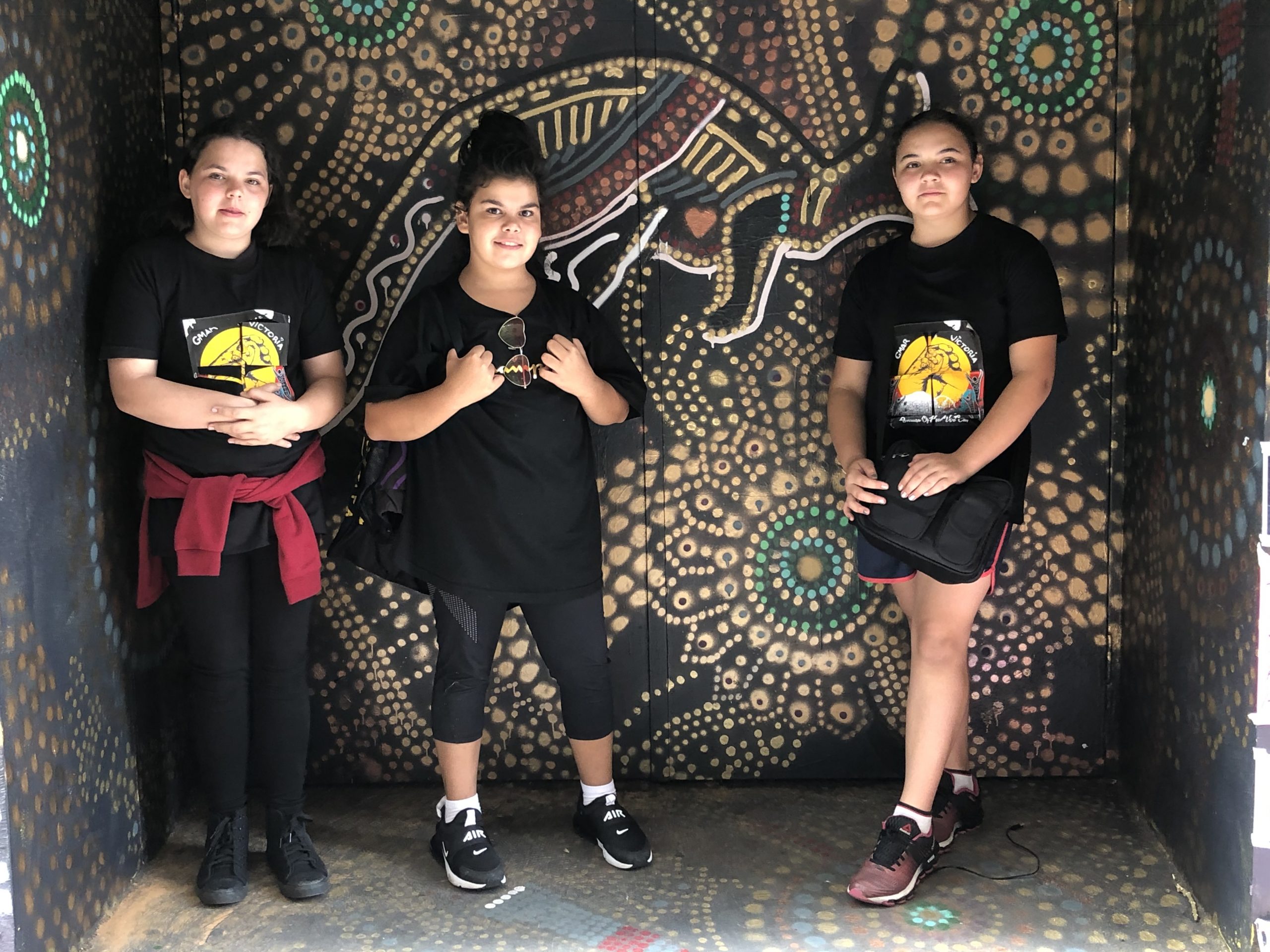3 girls dressed in black with aboriginal art work in the background