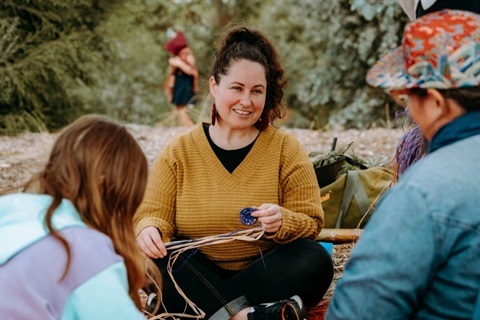 Woman in a yellow top sitting with others facing her, weaving outside.